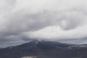 A scenic mountain in Spain, crowned with a dusting of snow. Cloudy sky add dramatic atmosphere.
