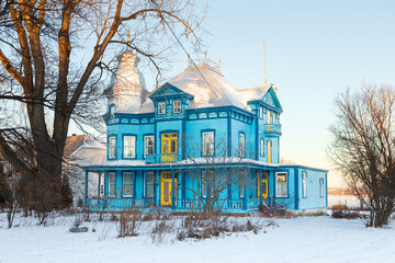 Blue Victorian house with metal sheet steep roof, yellow doors and turret railing seen during a winter morning, Saint-Antoine-de-Tilly, Quebec, Canada © Anne Richard