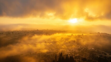 Naklejka premium Golden sunrise illuminating a hazy Jerusalem skyline surrounded by dramatic clouds and soft morning light