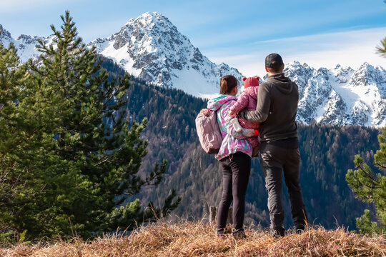 Father and mother with small child on top of Monte Nebria Est with panoramic view of snow capped mountains of Julian Alps, Friuli Venezia Giulia, Italy. Family hike in alpine wilderness in spring