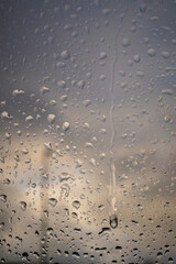 Rain drops on a window indicating gray and rainy day with defocused clouds and colors in background