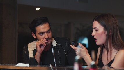 Portrait of focus beautiful woman talking with couple while looking at smartphone with serious face at bar. Capturing natural face beauty with dressing up social interaction at night club. Vinosity.