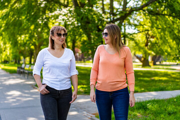Two mature beautiful women walking and talking in city park