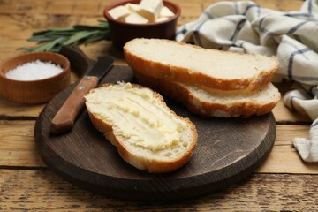 Fresh bread with butter and knife on wooden table, closeup