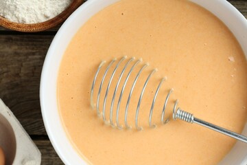 Bowl with dough for pumpkin pancakes and whisk on wooden table, closeup