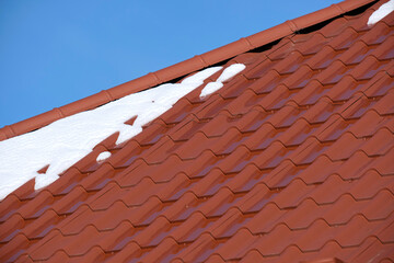 Naklejka premium Closeup of house roof top covered with snow in cold winter. Tiled covering of building in wintertime weather