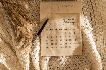 Minimal top view aesthetic composition with beige linen fabric calendar with January month 2025, pen and dry branch on a knitted blanket. Flat lay, New Year template
