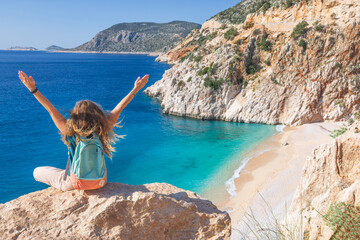 Obraz premium Young woman with backpack looking out over Kaputas beach, Lycia coast. Summer day walk by Lycian way at family vacation in Mediterranean Sea, Kas, Antalya region, Turkey
