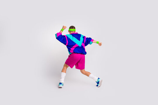 Energetic young man in vibrant retro activewear performing a dynamic exercise against a white grey background