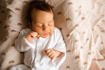 Cute baby boy 1-2 months old wearing pajamas sleeping in bed close up top view. Good morning. Childhood.