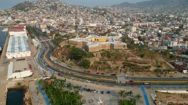 Aerial video moving in reverse from the Fort of San Diego towards Parque de la Reina in Acapulco, showcasing the coastal view