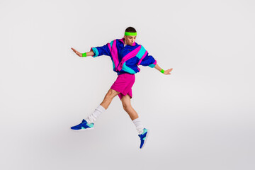 Obraz premium Young man in vibrant retro sportswear leaping mid-air against white background, showcasing dynamic athletic movement and 80s fashion style