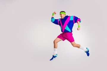 Fototapeta premium Young man in colorful retro outfit jumps energetically against a white background, showcasing vibrant fashion and dynamic movement