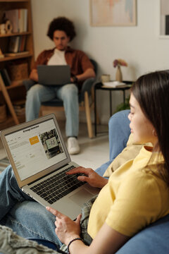Young female designer creating new content in AI image generator while using laptop against her boyfriend