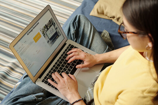 High angle of young creative female specialist using AI image generator while pressing laptop keys