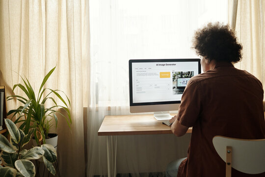 Rear view of young male designer sitting in front of desktop compuer screen with visual language model