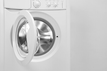 Washing machine with empty drum near light wall, closeup. Space for text