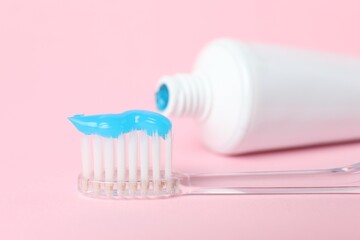 Toothbrush with toothpaste and tube on pink background, closeup