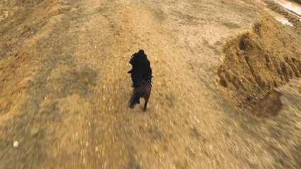 In ancient times, a black-dressed person riding a horse across a barren land. an Arab riding a horse. Generative AI - Powered by Adobe