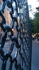 Naklejka premium Close-up of a dark metal chain-link fence, city buildings and trees in the blurry background.
