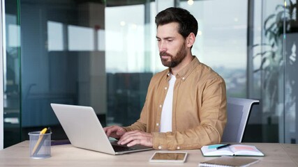 Focused handsome businessman typing on a laptop sitting at a workplace in a business office. Bearded male worker working in computer, banking, texting a client, chatting online or busy with a project - Powered by Adobe