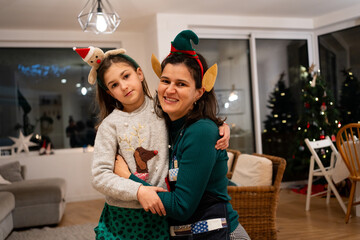 smiling portrait of mother in apron and daughter in dining room decorated for Christmas with reindeer and elf headband