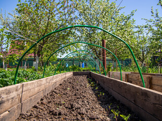 A bed with a fence made of wooden boards and arches for a mini-greenhouse