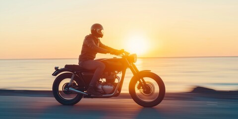 Fototapeta premium A man is riding a motorcycle on a road near the ocean. The sun is setting in the background, creating a beautiful and serene atmosphere