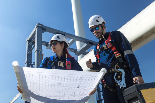 Inspection engineers a rotor blade of a wind turbine. Professional Man Maintenance engineers working in wind turbine farm. Engineer Man standing among Wind Energy Turbine. - Powered by Adobe