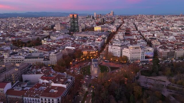 Breathtaking aerial view of Madrid, iconic El Retiro Park and historic Puerta de Alcala, contrasting rich history with modernity amidst bustling traffic with stunning purple blue sunset sky 