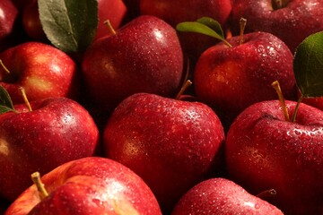 Fresh ripe red apples and green leaves as background, closeup
