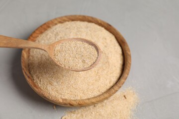 Oat bran in wooden spoon over bowl at grey table, closeup