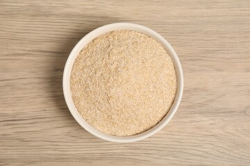 Oat bran in bowl on wooden table, top view