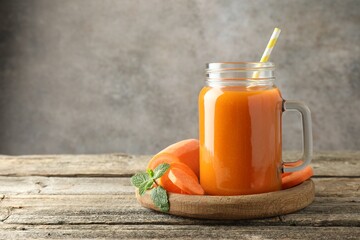 Fresh carrot juice in mason jar, vegetable and mint on wooden table against gray background, space...