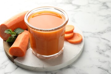 Fresh carrot juice in glass, vegetables and mint on white marble table, closeup