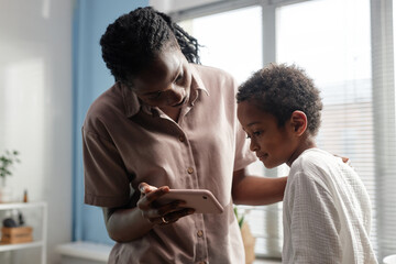Obraz premium Black Woman Holding Phone while Little Son Looking at Smartphone Screen in Bathroom