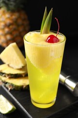 Fototapeta premium Tasty pineapple cocktail with cherry in glass on black table, closeup