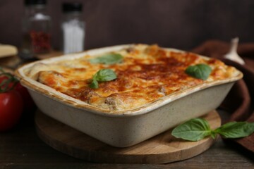 Delicious cooked lasagna in baking dish and basil on wooden table, closeup