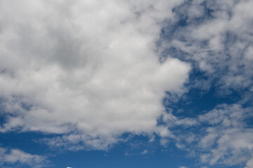 Obraz premium Fluffy white clouds float lazily in a clear blue sky, creating a picturesque backdrop. The sun shines brightly, enhancing the peaceful atmosphere of the scene