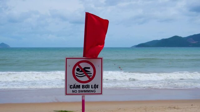 Red flag and sign swimming is prohibited on the beach during powerful life threatening surf waves. Inscription - Do not swim