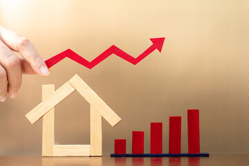 Woman hand hold a red arrow graph with grow value to home model put and bar graph with growing value put on the desk in the office, Buy or sell a house and real estate for working capital concept.