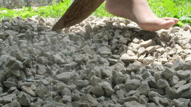 Close Up shot footage of a hoe leveling split stones to cover the yard. Compacting the soil with stones for the Gardening Industry. Garden Decoration. A man is hoeing.