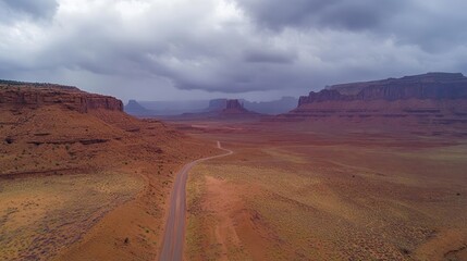 Aerial view of a desert road winding through red rock formations under a dramatic sky.
