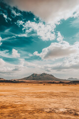 Expansive desert landscape with dramatic clouds and distant mountains under a blue sky