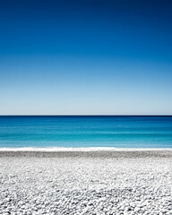 Obraz premium Scenic view of a tranquil beach with pebbles under a clear blue sky