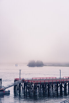 A foggy morning in a Pacific Ocean bay with a boat coming out of the gloom and a pier deck on the foreground