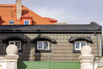 detail of building facade behind green wooden fence with red and black tiles
