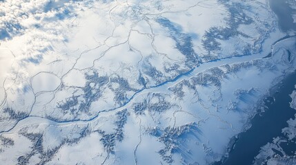 An overhead perspective of a frozen river, with geometric patterns formed by cracks in the ice and patches of snow scattered across