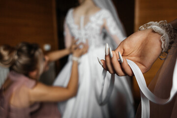 wedding preparation scene. In the foreground is a woman's hand with long silver nails holding a...