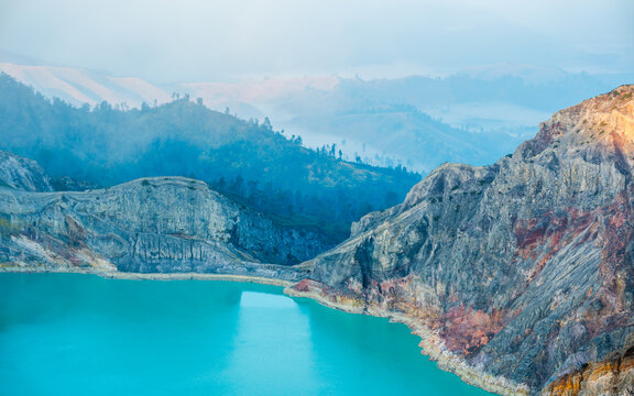 Volcano mountain with a scenic sulfur lake surrounded by mist and clouds at sunrise, Kawah Ijen, Java, Indonesia.